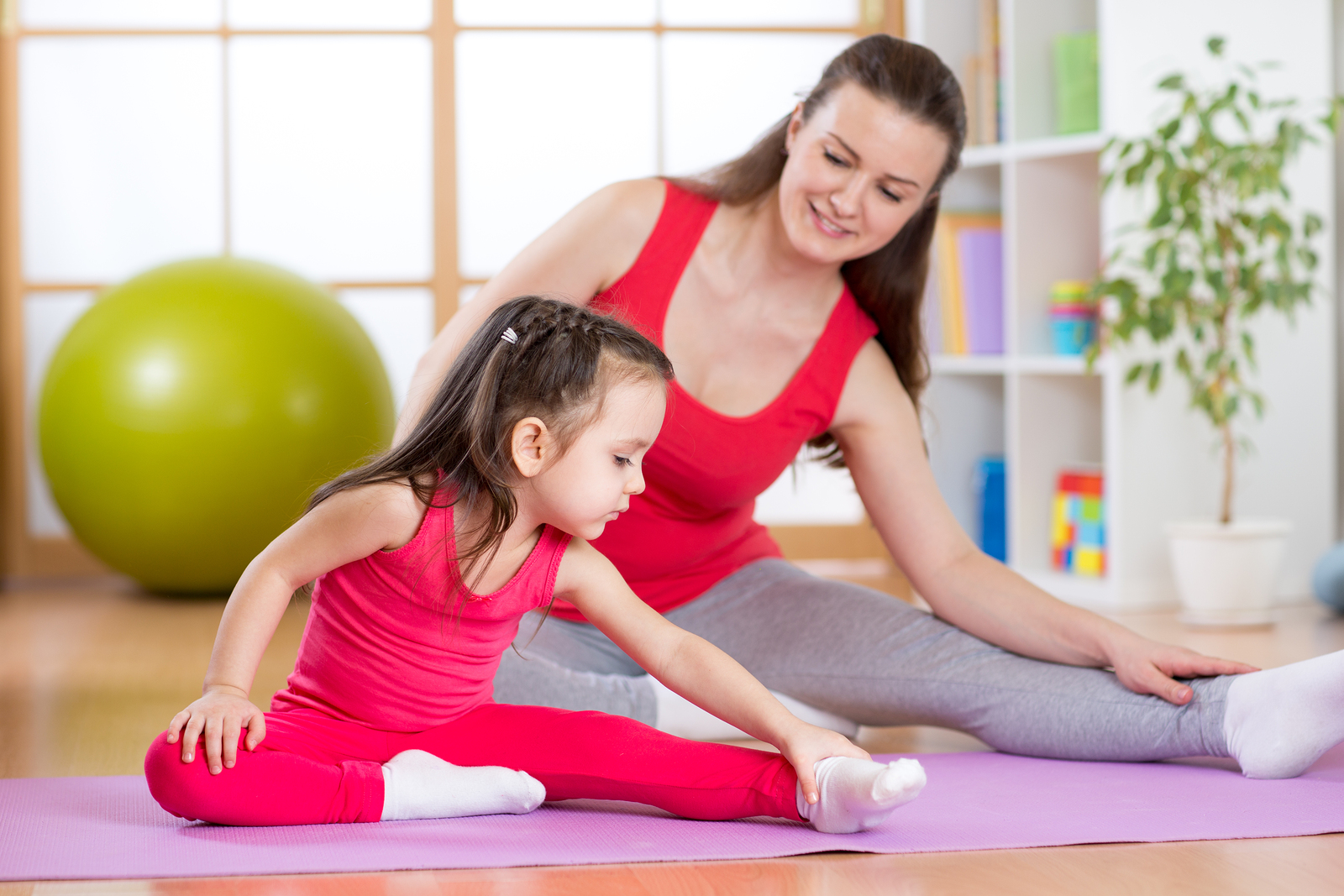 Mother and daughter doing fitness exercises on mat at home - Go Mommy